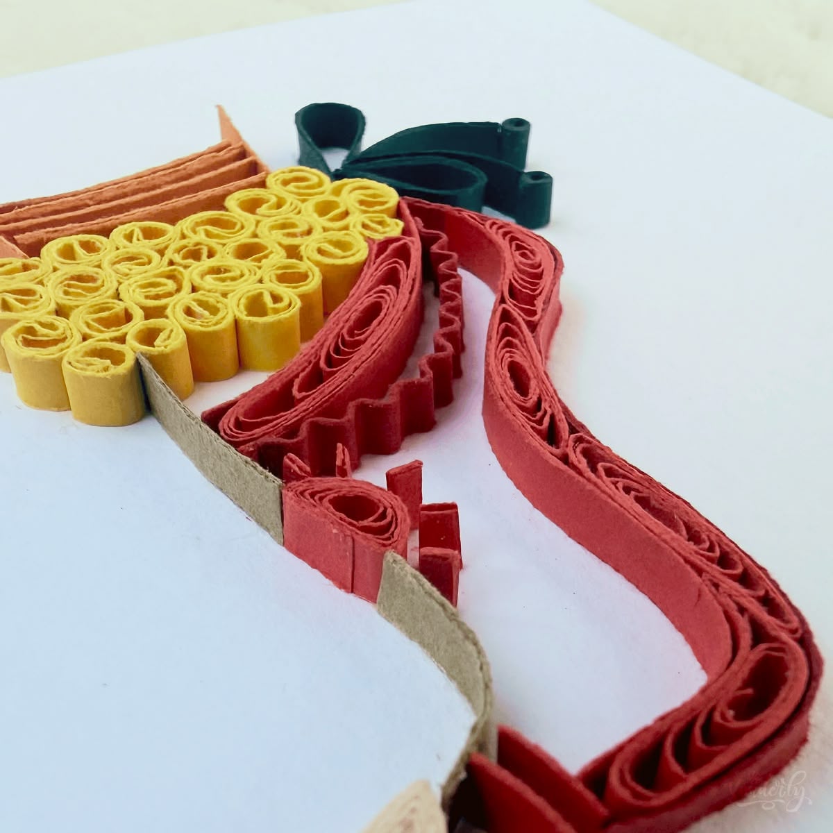 Angled view of quilled Bharatanatyam dance card showing 3D raised paper art, ankle bells cluster and red leg detail visible