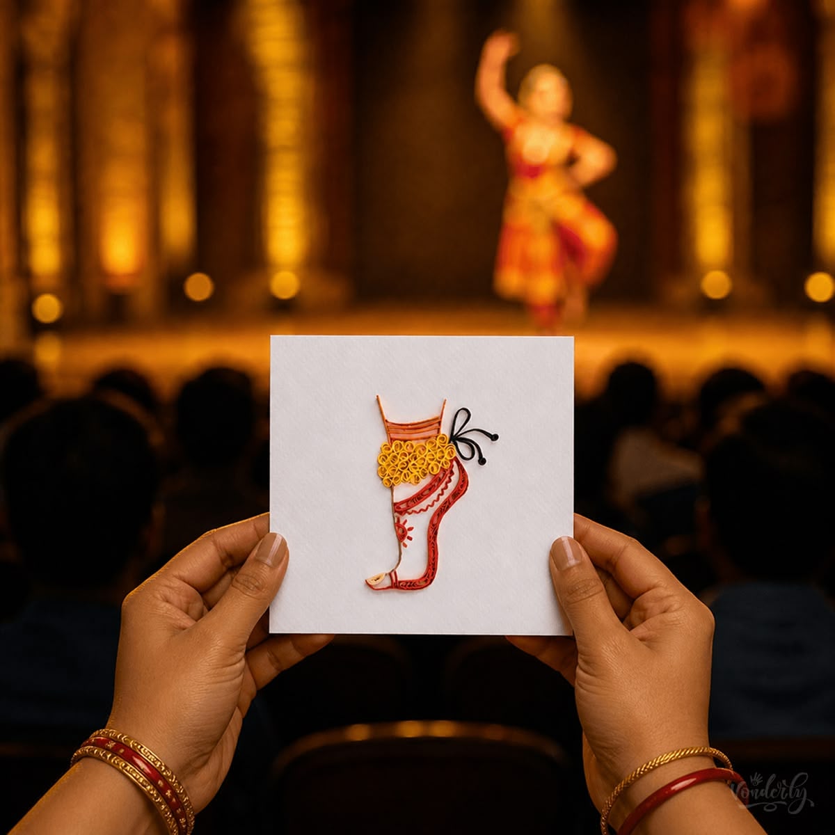 Audience member holds handmade quilled Bharatanatyam dance card as classical dancer performs on stage, Vonderly