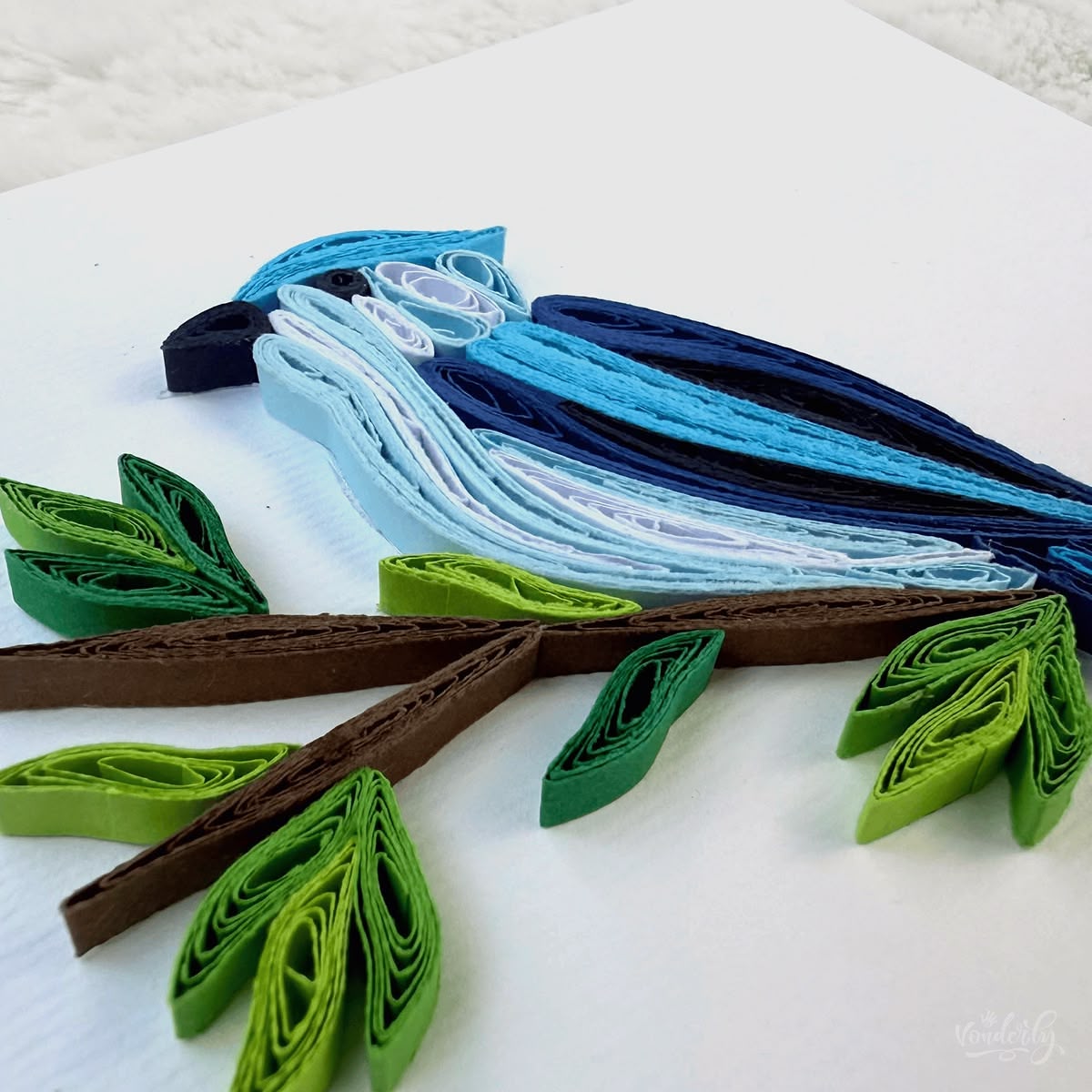 Angled view of quilled blue jay card showing 3D raised paper art, layered blue feathers and branch detail visible