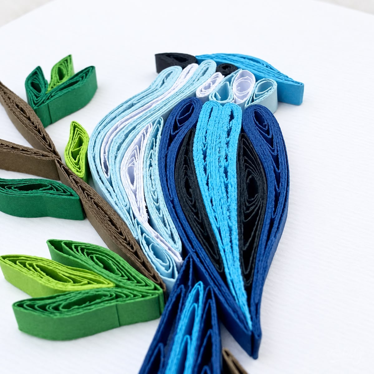 Close-up of light blue, mid blue, and navy paper strips forming the blue jay's wing and tail.