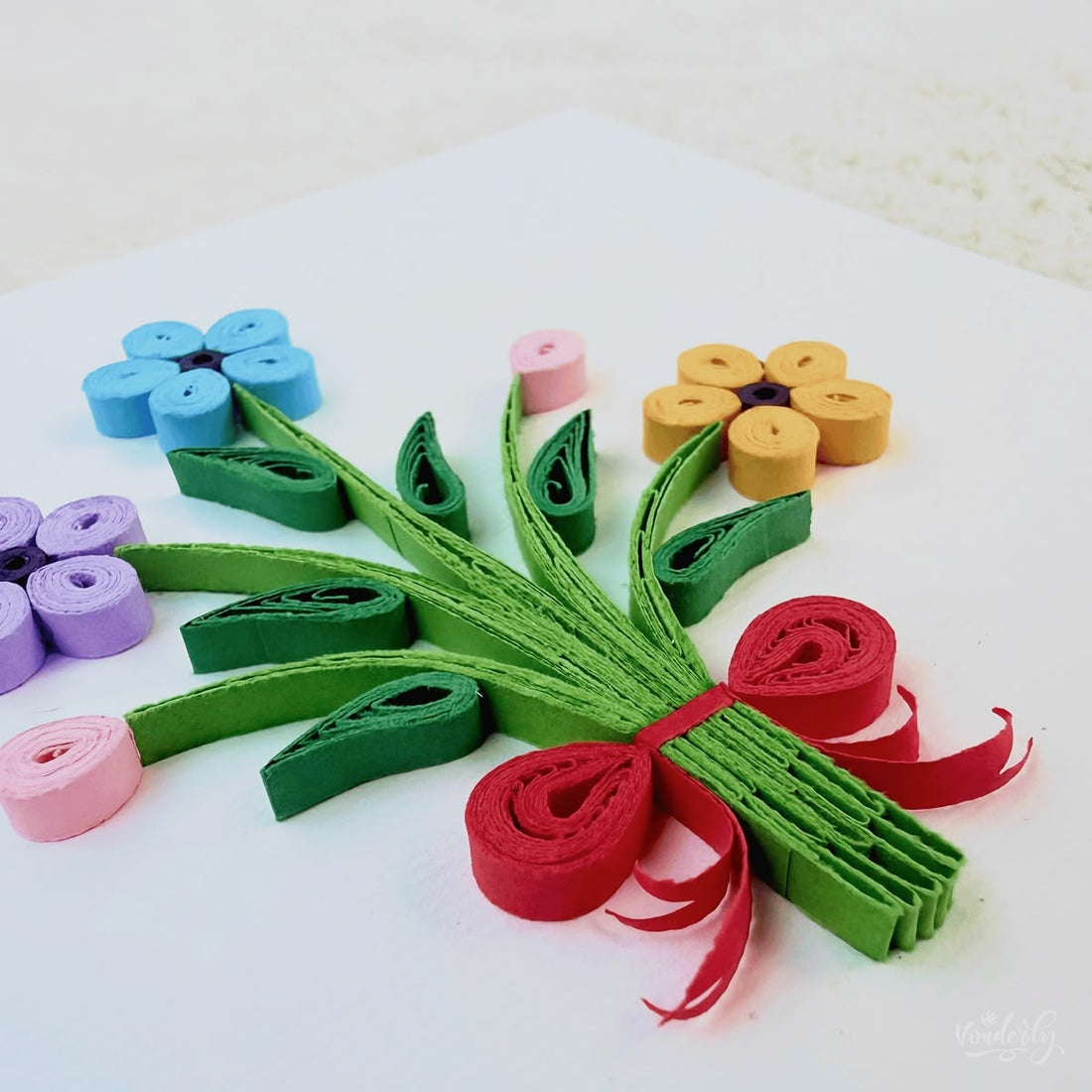 Handmade quilled flower bouquet greeting card, three flowers (blue, lavender, orange) with two pink buds on gathered green stems tied with a red ribbon, paper art by Vonderly
