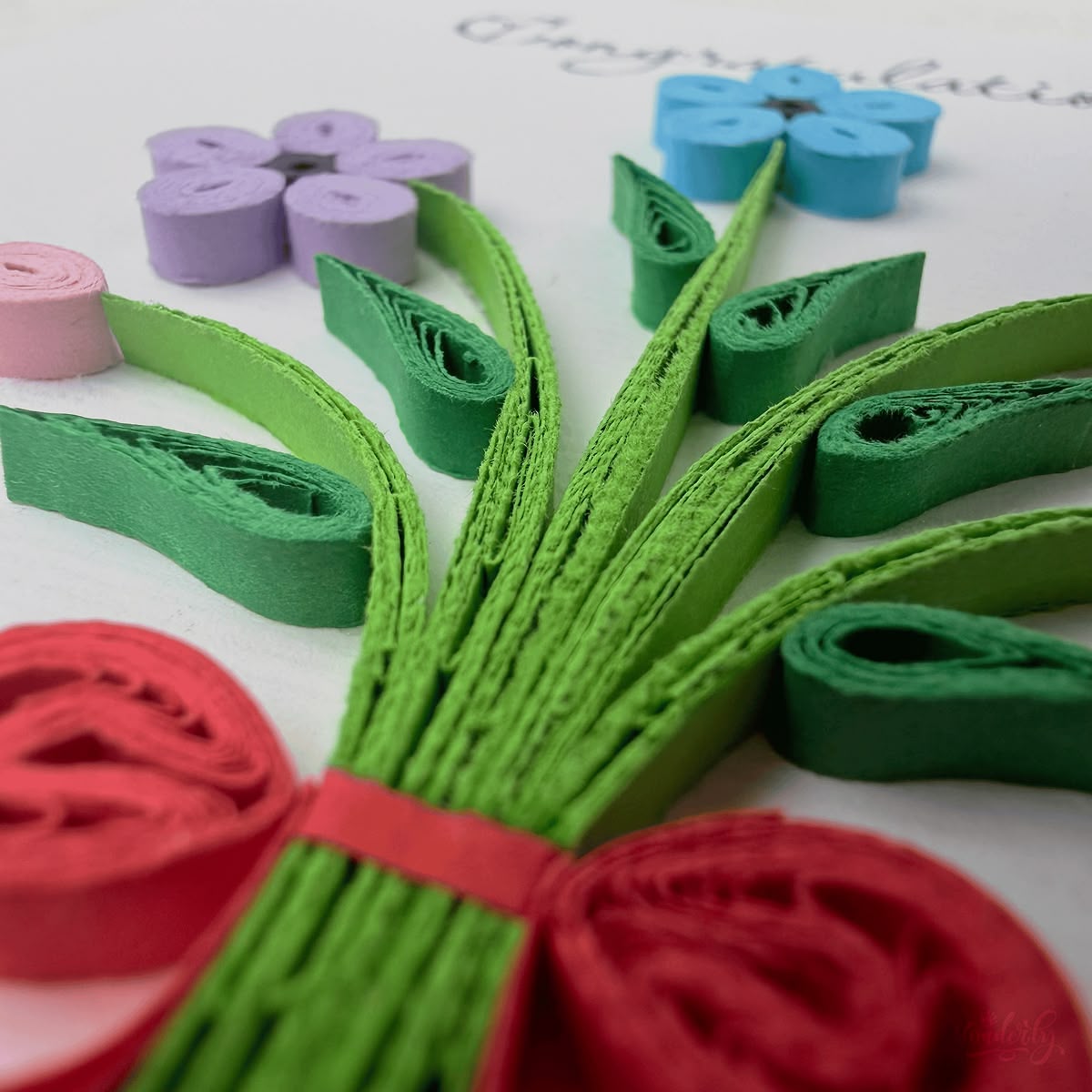 Close-up macro of paper quilling on congratulations bouquet card, ribbon bow and stem bundle with adjacent flower elements