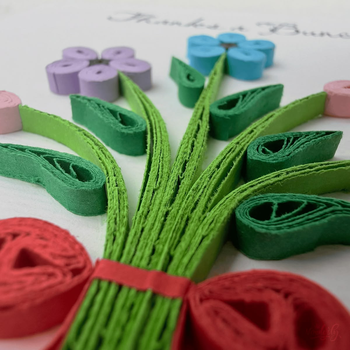 Close-up macro of paper quilling on thank you bouquet card, gathered green stems and red ribbon tie with adjacent flower elements