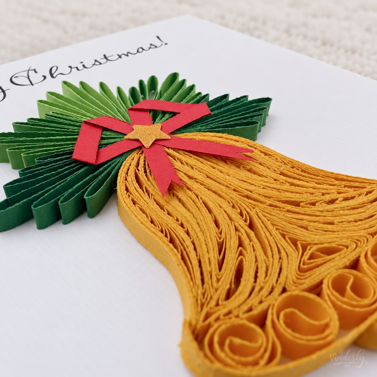 Angled view of the Christmas Bell card showing the looped gold strips and folded green pine sprays.