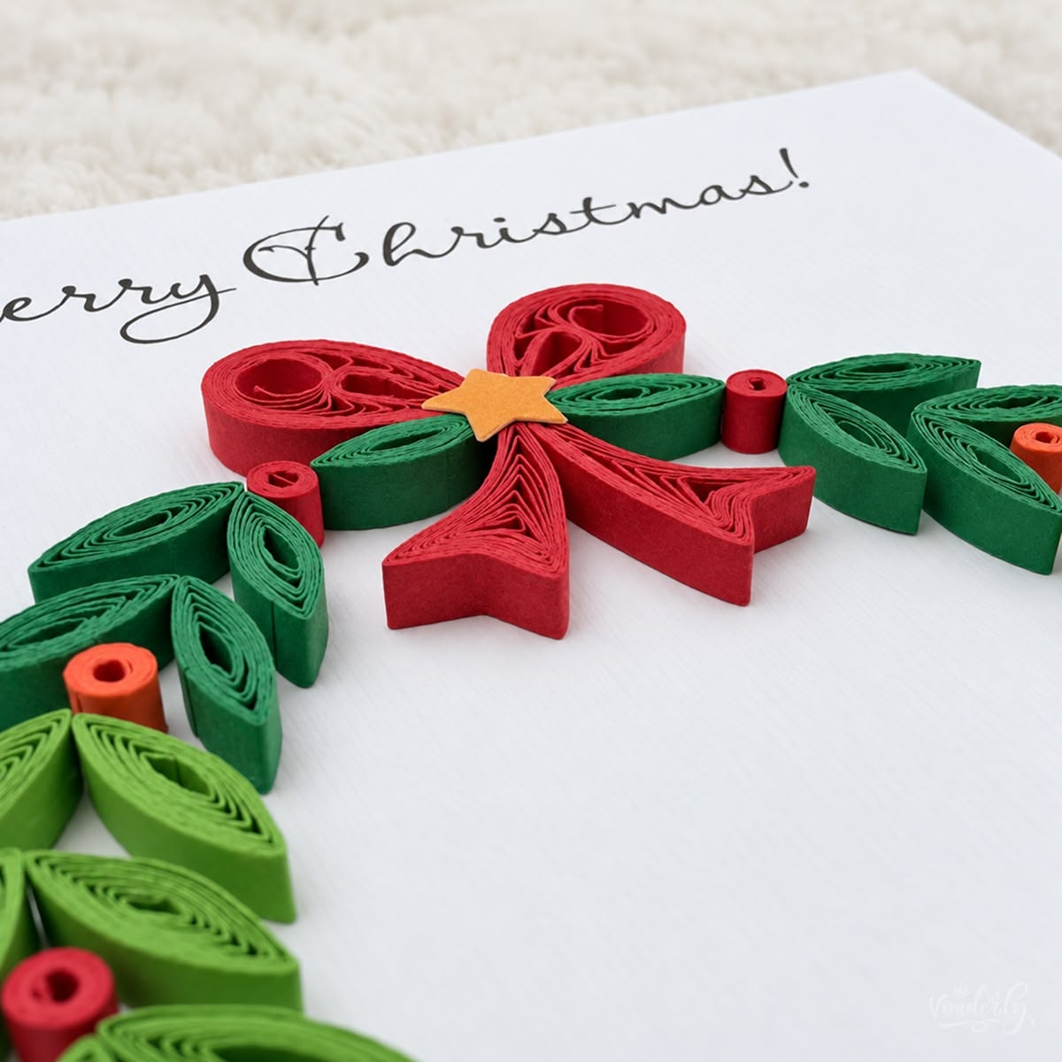 Close-up of a red paper bow coiled above green leaves and small red and orange berries.