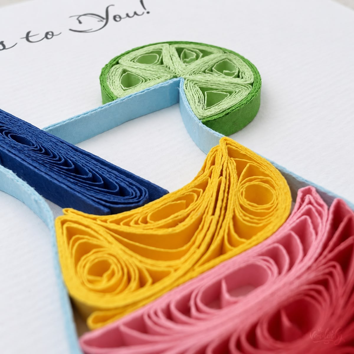 Close-up of a green paper lime wheel and yellow strips coiled into a drink layer.