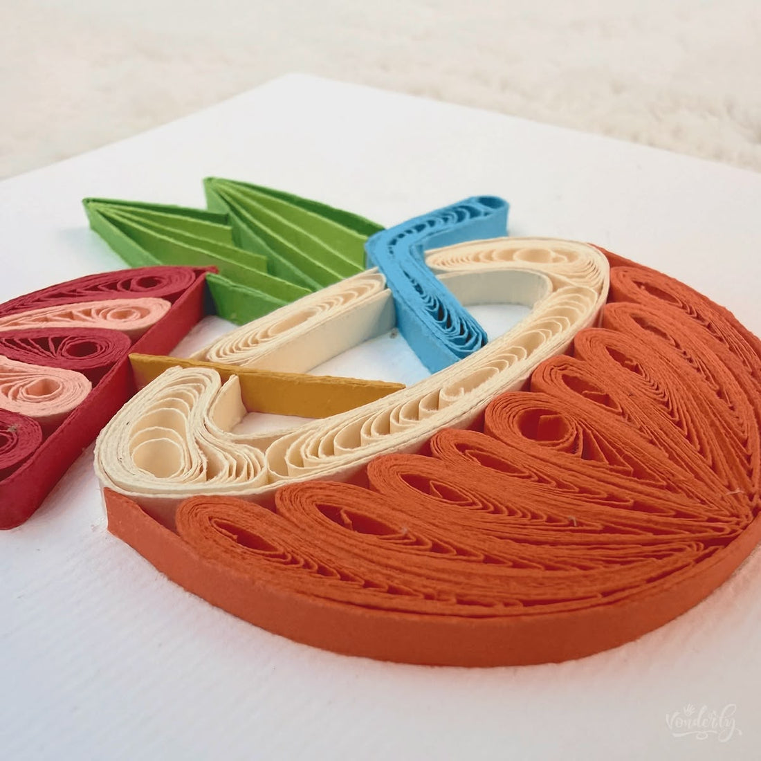 Handmade quilled tropical greeting card showing a halved orange coconut with a cream drink, red and pink cocktail umbrella, blue straw, and green leaves, paper art by Vonderly
