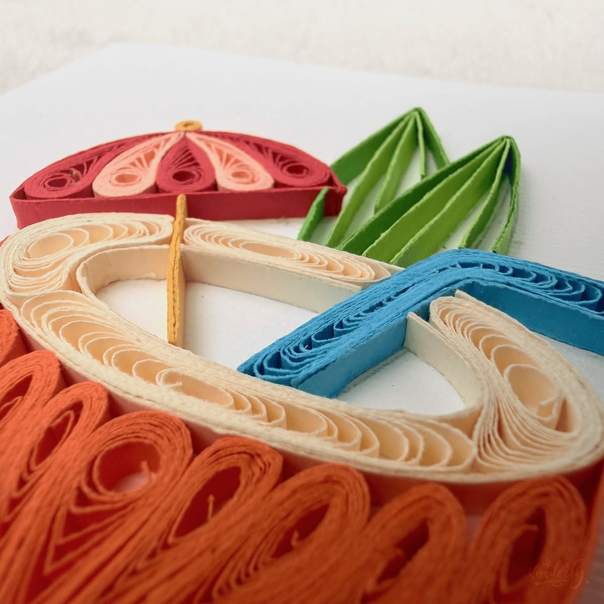 Close-up macro of paper quilling on the coconut drink card, tight orange coils of the shell, cream scrolled rim, red umbrella panels, and green husked leaves