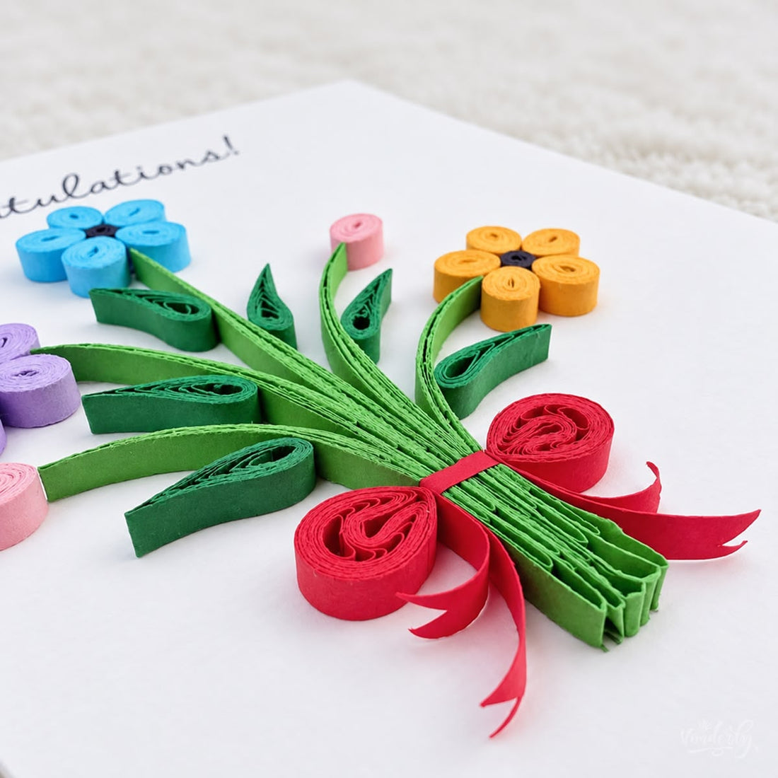 Congratulations greeting card with a quilled bouquet in blue, purple, and yellow paper flowers under black script.