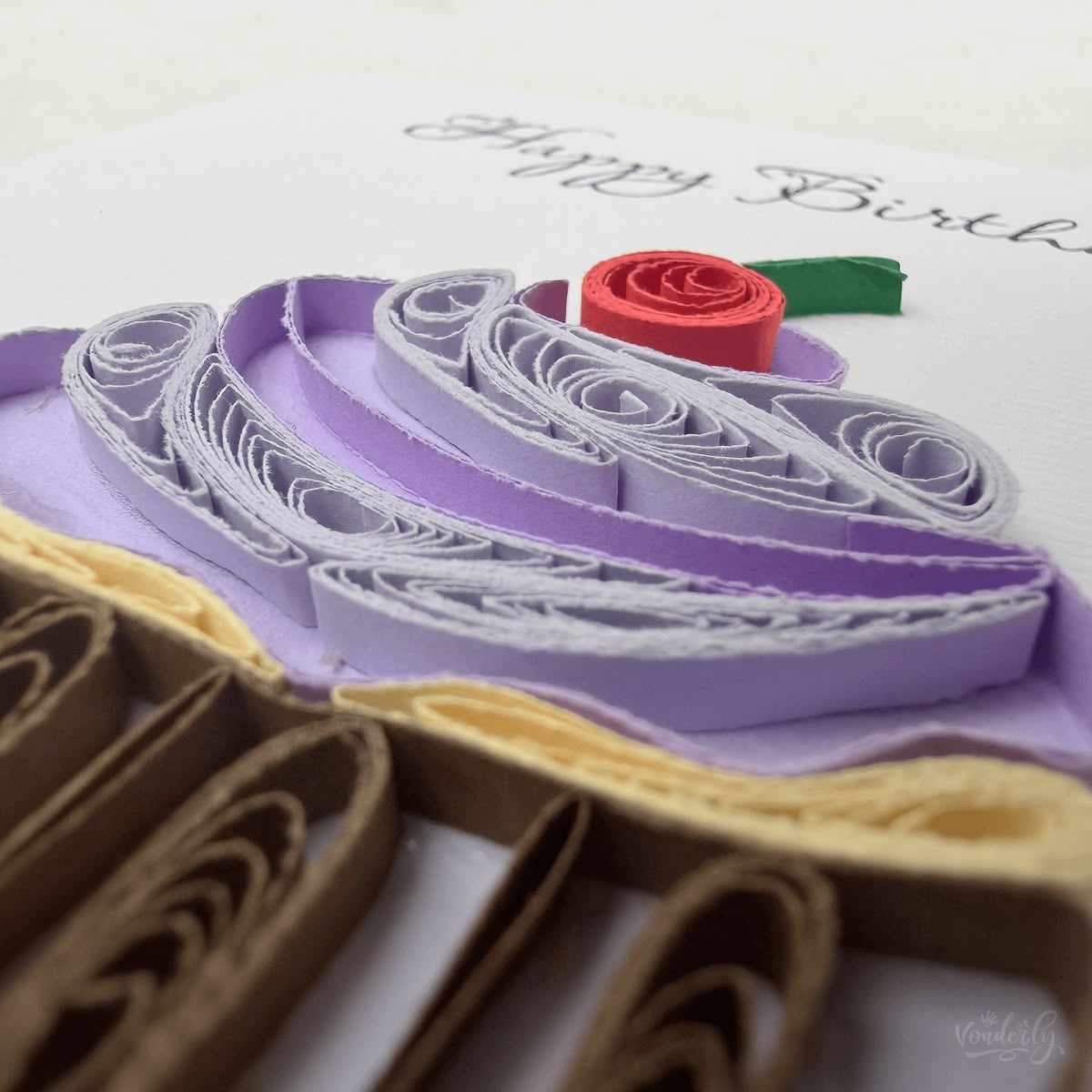 Close-up macro of paper quilling on the cupcake birthday card, piped frosting swirl with fine inner scrollwork, tight striped wrapper coils, and red cherry