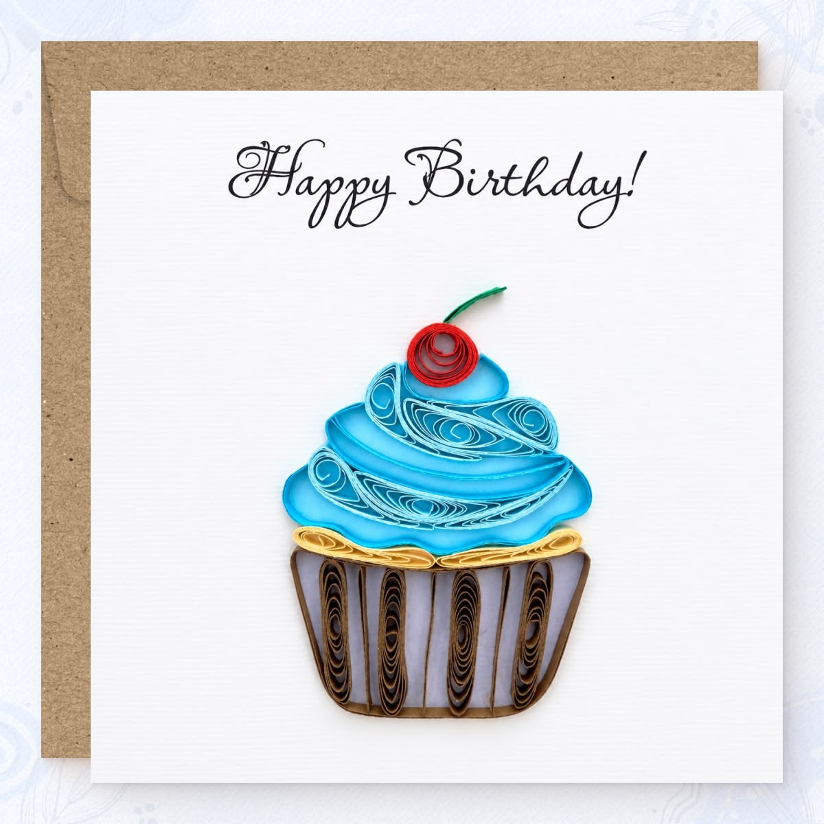 Quilled birthday card with a blue paper frosting swirl, red cherry, and striped wrapper.