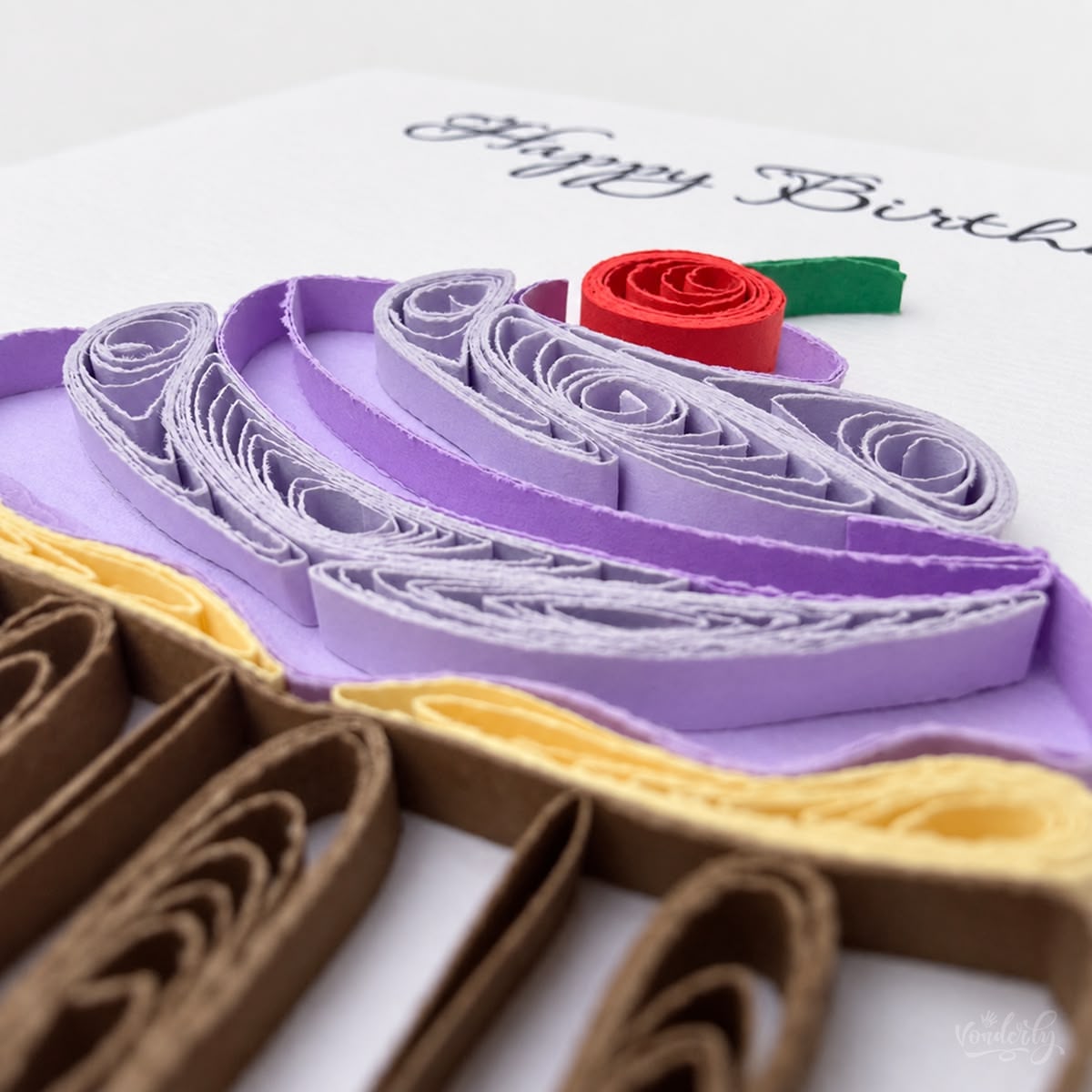Close-up of paper strips coiled into a frosting swirl beside a rolled red cherry.
