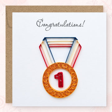 Quilled congratulations card with a gold paper medal and red number 1 on a navy, cream, and red ribbon.