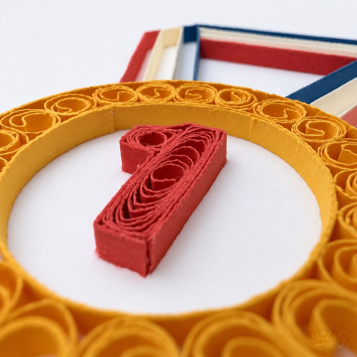 Close-up of tightly rolled gold coils forming the medal ring around a red paper numeral.