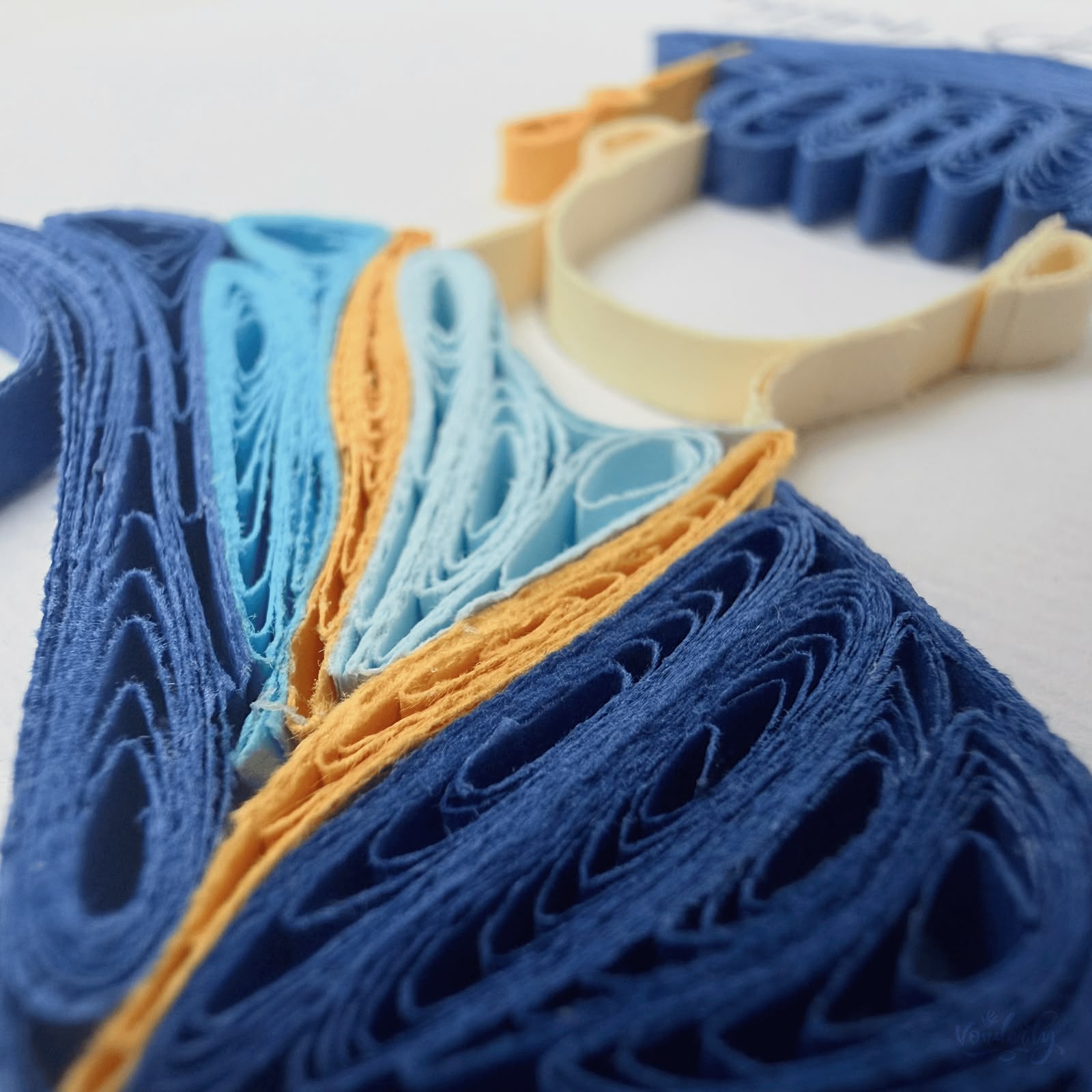 Close-up macro of paper quilling on graduation card, navy blue and light blue coils with gold trim paper strips