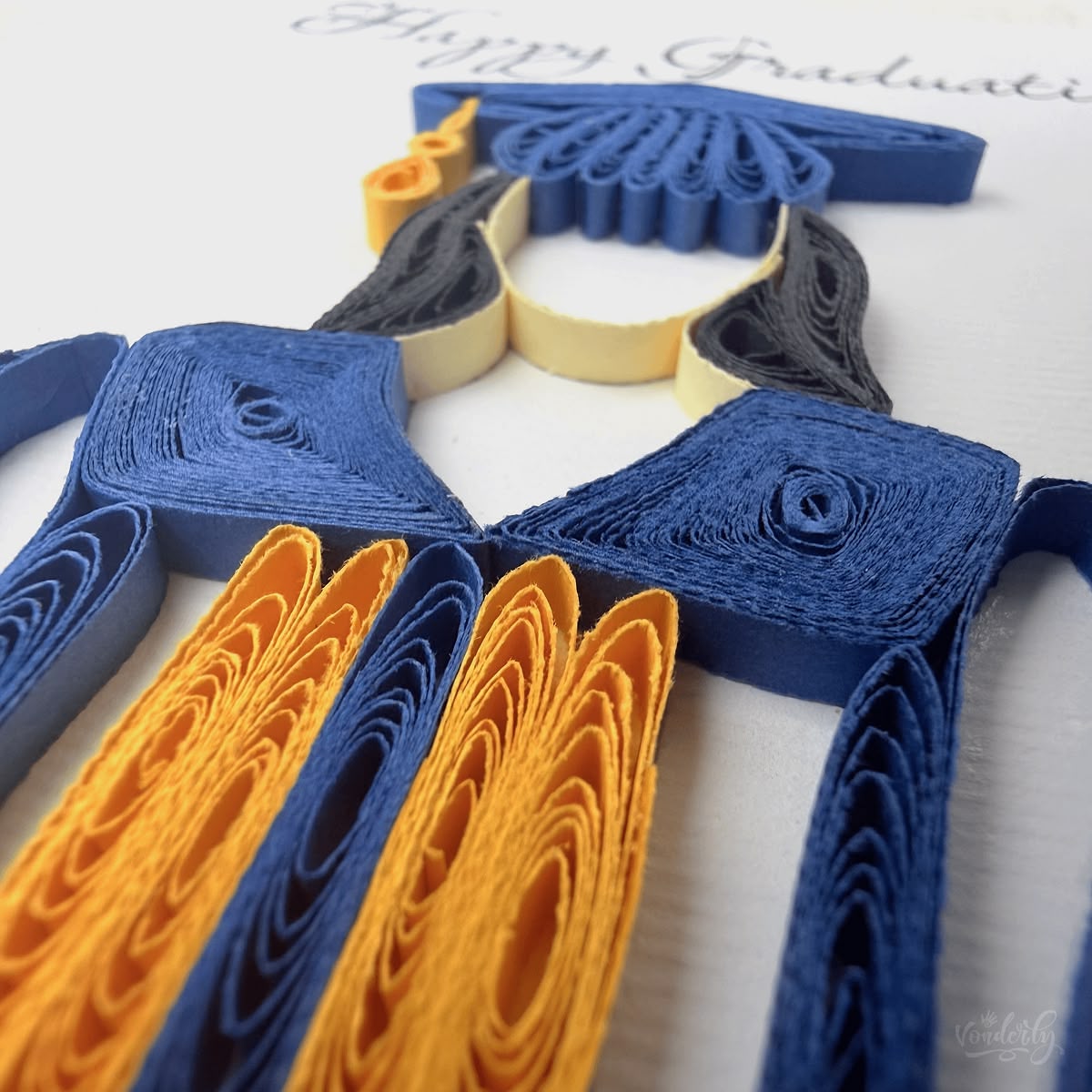 Close-up macro of paper quilling on graduation card, navy gown collar and gold stole strips visible