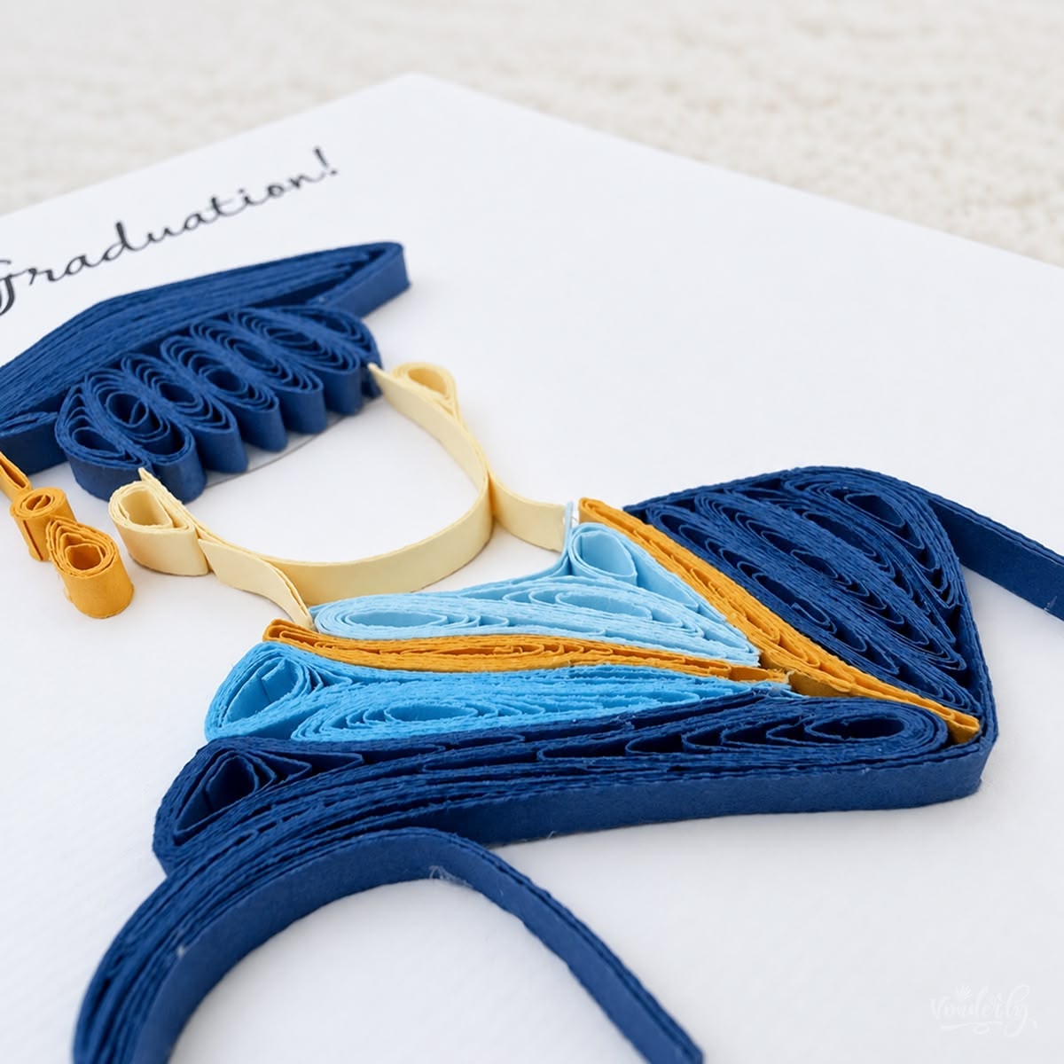 Angled view of the graduation card showing the raised navy gown strips and the layered hood.