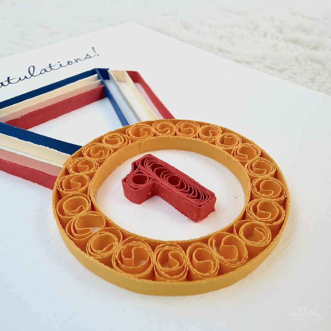 Handmade quilled congratulations greeting card with a gold first-place medal and number 1 hanging on a multi-colored ribbon, "Congratulations" printed in calligraphic script, paper art by Vonderly