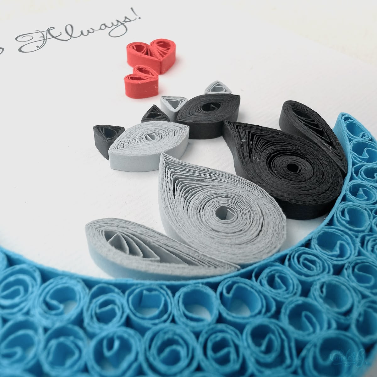 Close-up macro of paper quilling on anniversary card, two cats and red hearts against the blue crescent moon coil-by-coil construction