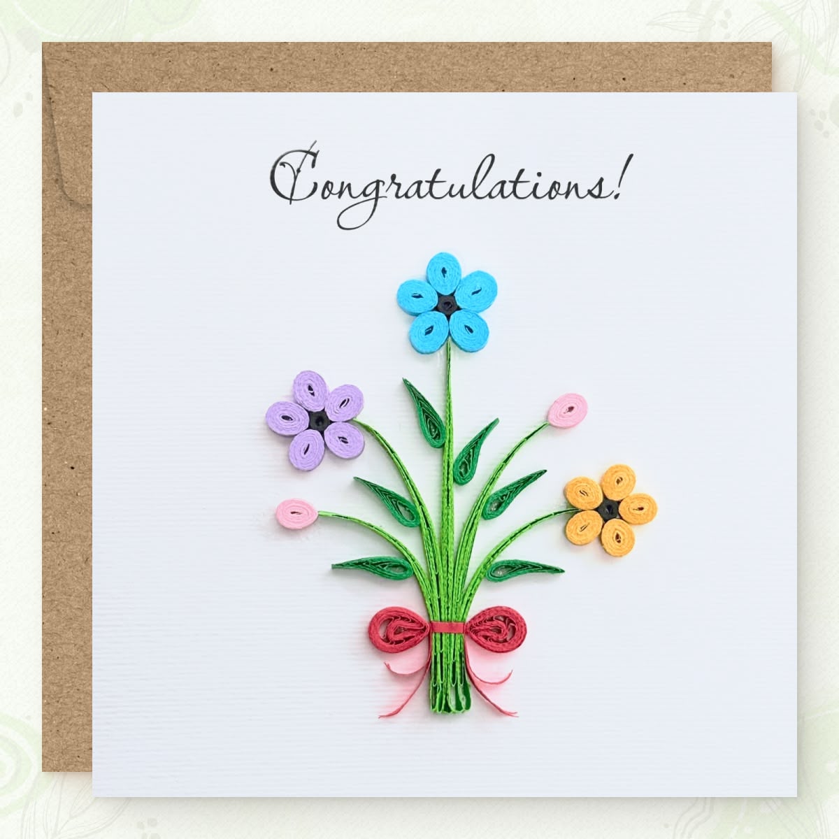 Handmade quilled congratulations greeting card with three flowers (blue, lavender, orange), two pink buds, and a red ribbon bow on gathered green stems, "Congratulations" printed in calligraphic script, paper art by Vonderly