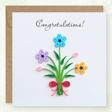 Handmade quilled congratulations greeting card with three flowers (blue, lavender, orange), two pink buds, and a red ribbon bow on gathered green stems, "Congratulations" printed in calligraphic script, paper art by Vonderly