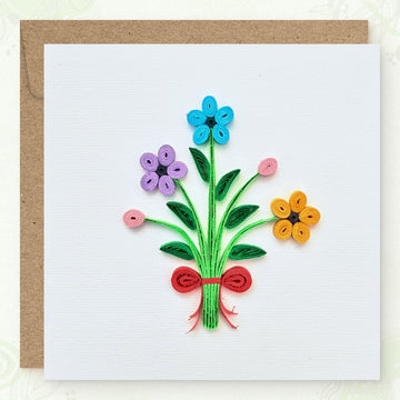 Handmade quilled flower bouquet greeting card, three flowers (blue, lavender, orange) with two pink buds on gathered green stems tied with a red ribbon, paper art by Vonderly