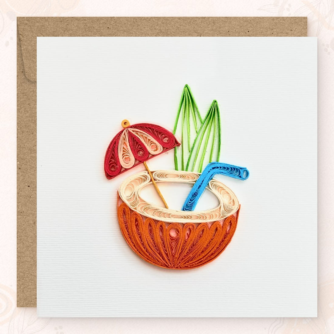 Handmade quilled tropical greeting card showing a halved orange coconut with a cream drink, red and pink cocktail umbrella, blue straw, and green leaves, paper art by Vonderly