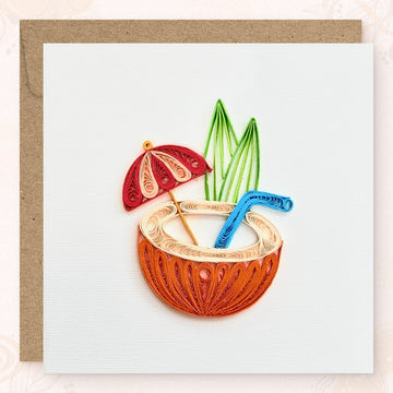 Handmade quilled tropical greeting card showing a halved orange coconut with a cream drink, red and pink cocktail umbrella, blue straw, and green leaves, paper art by Vonderly