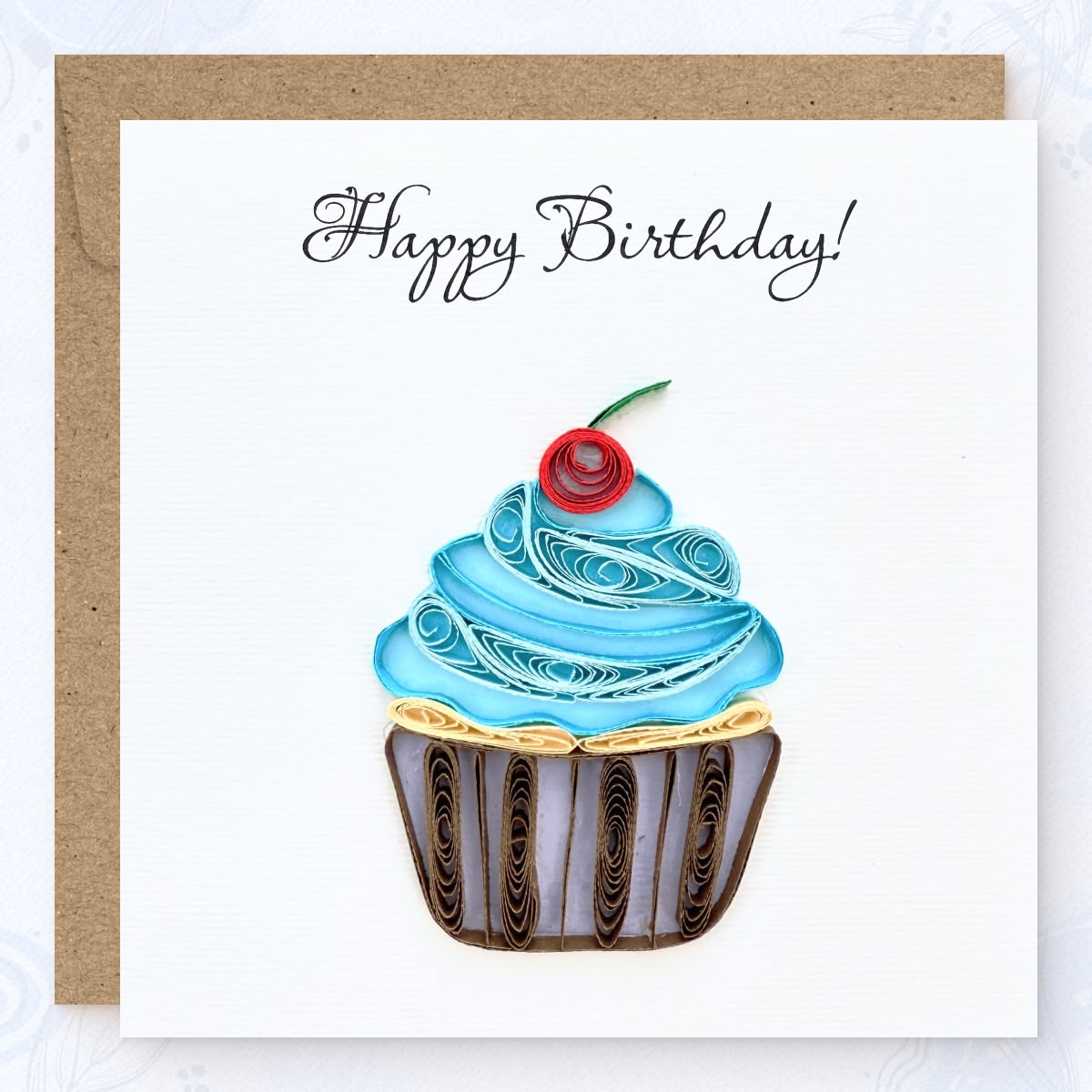 Handmade quilled birthday greeting card with a blue frosting cupcake, red cherry, and striped wrapper, "Happy Birthday" printed in calligraphic script, paper art by Vonderly