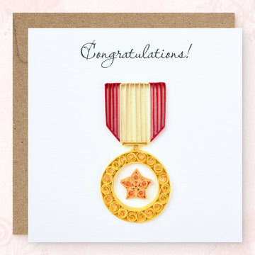 Handmade quilled congratulations greeting card with a gold service-style medal and orange star at its center, hanging from a red and cream striped ribbon, "Congratulations" printed in calligraphic script, paper art by Vonderly