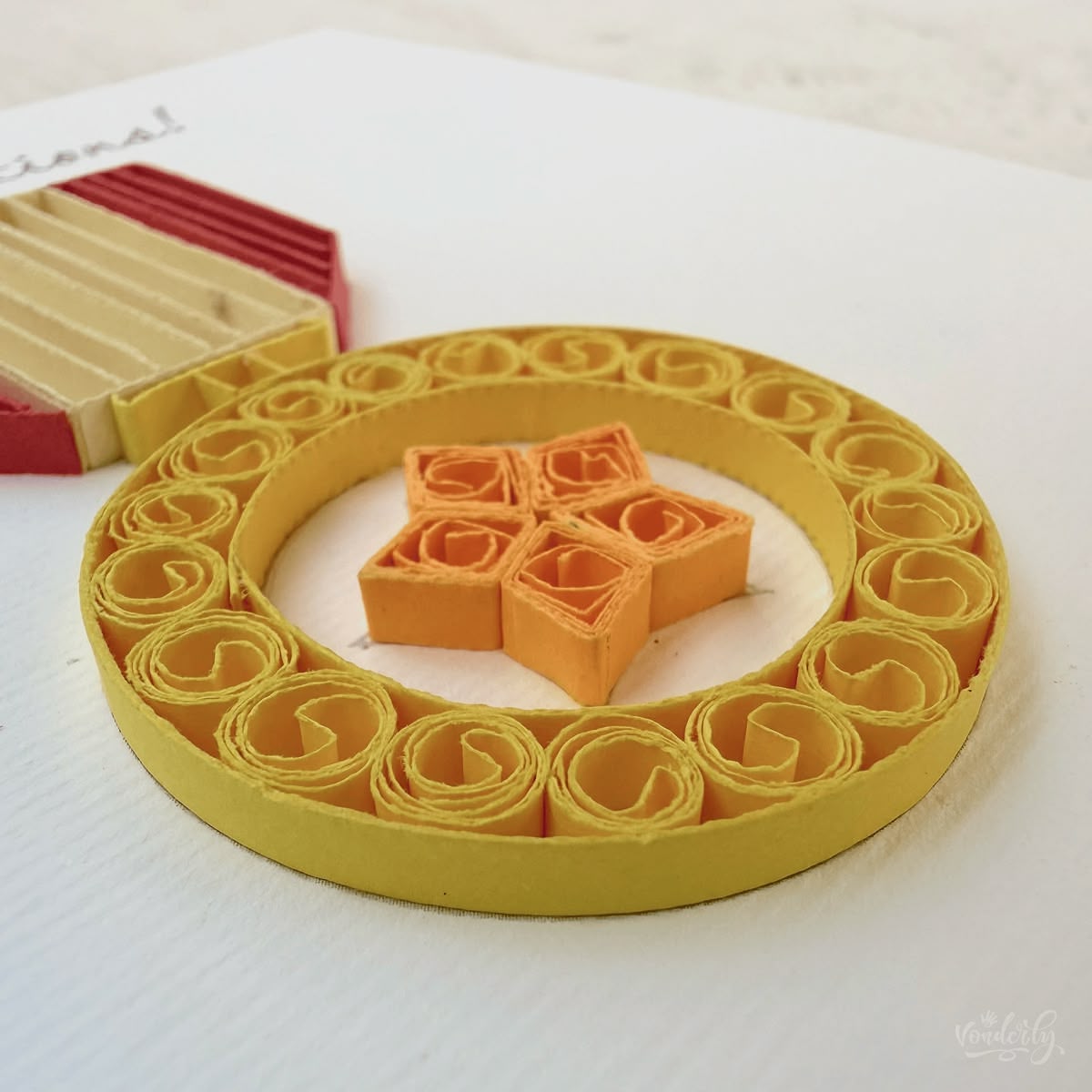 Angled view of quilled congratulations card showing 3D raised paper art, gold medal ring with orange star center and striped service ribbon visible