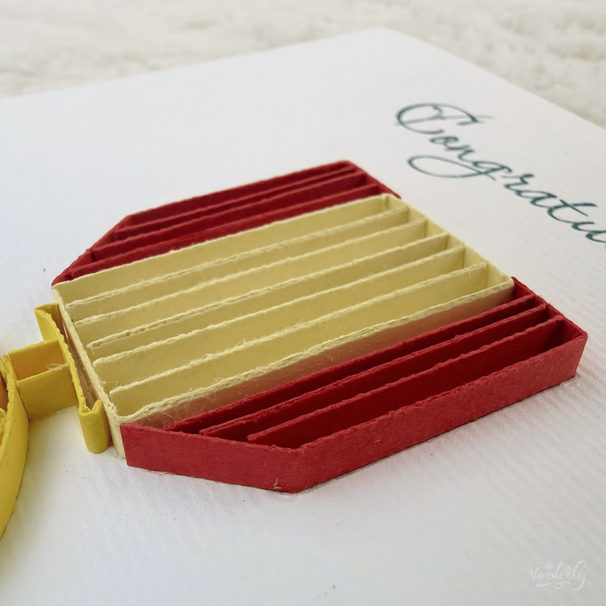 Close-up macro of paper quilling on star medal card, tightly rolled gold coils forming the medal ring and five pentagonal orange segments forming the central star
