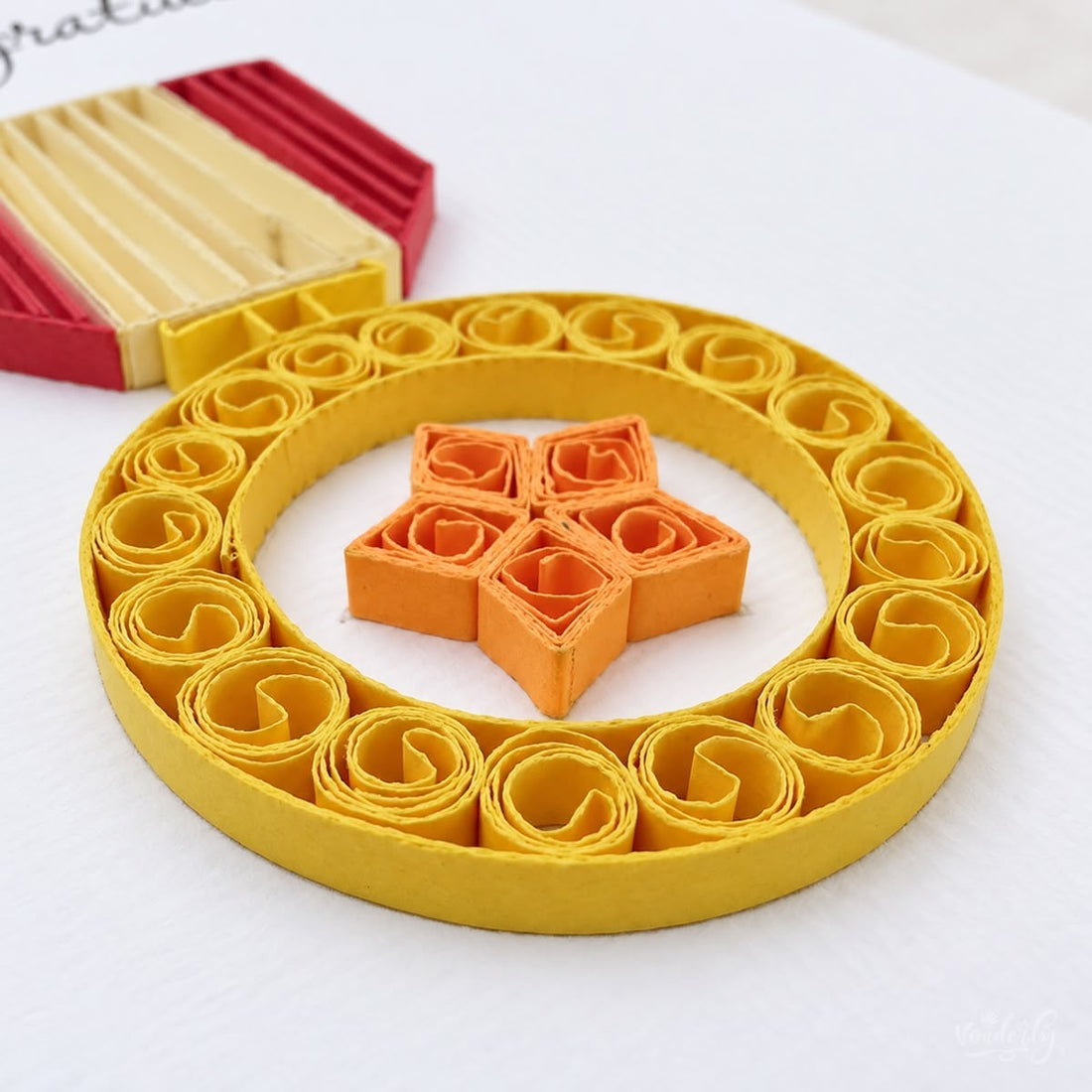 Quilled congratulations card with a gold paper medal, orange star, and a red and cream shield ribbon.