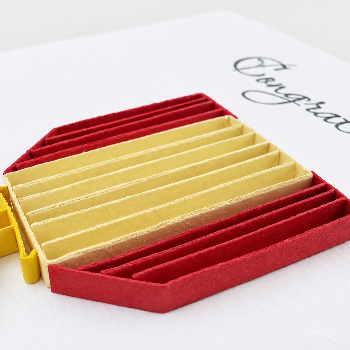 Close-up of red and cream paper strips stood on edge forming the shield ribbon of the medal.
