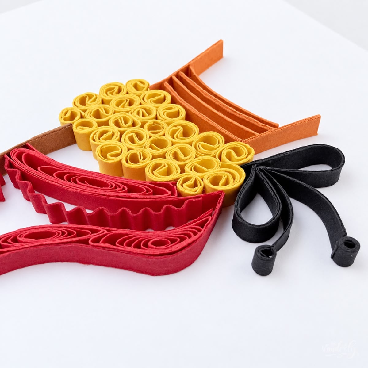 Close-up of tightly coiled gold paper forming the salangai beside red and coral strips set on edge.