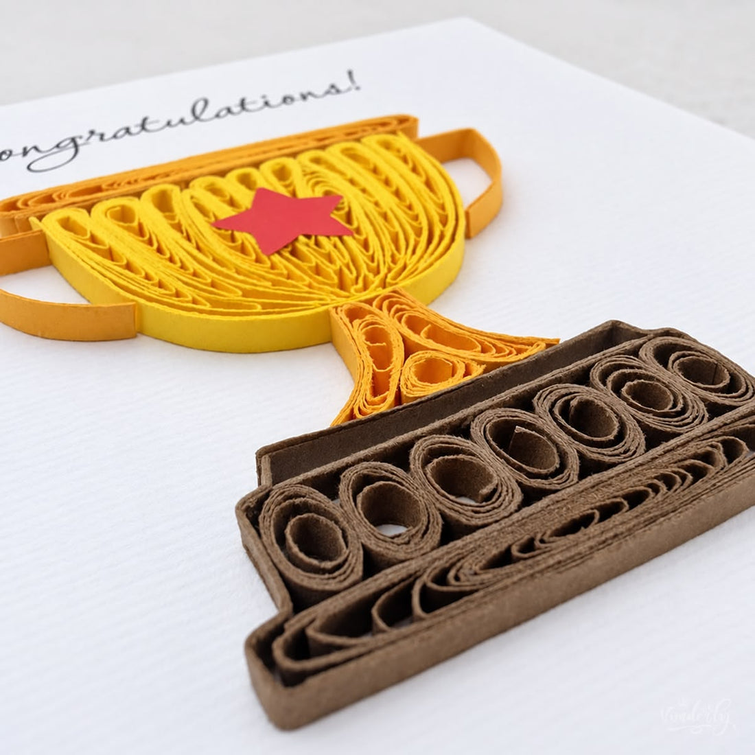 Quilled congratulations card with a gold paper trophy, red star, and brown base.