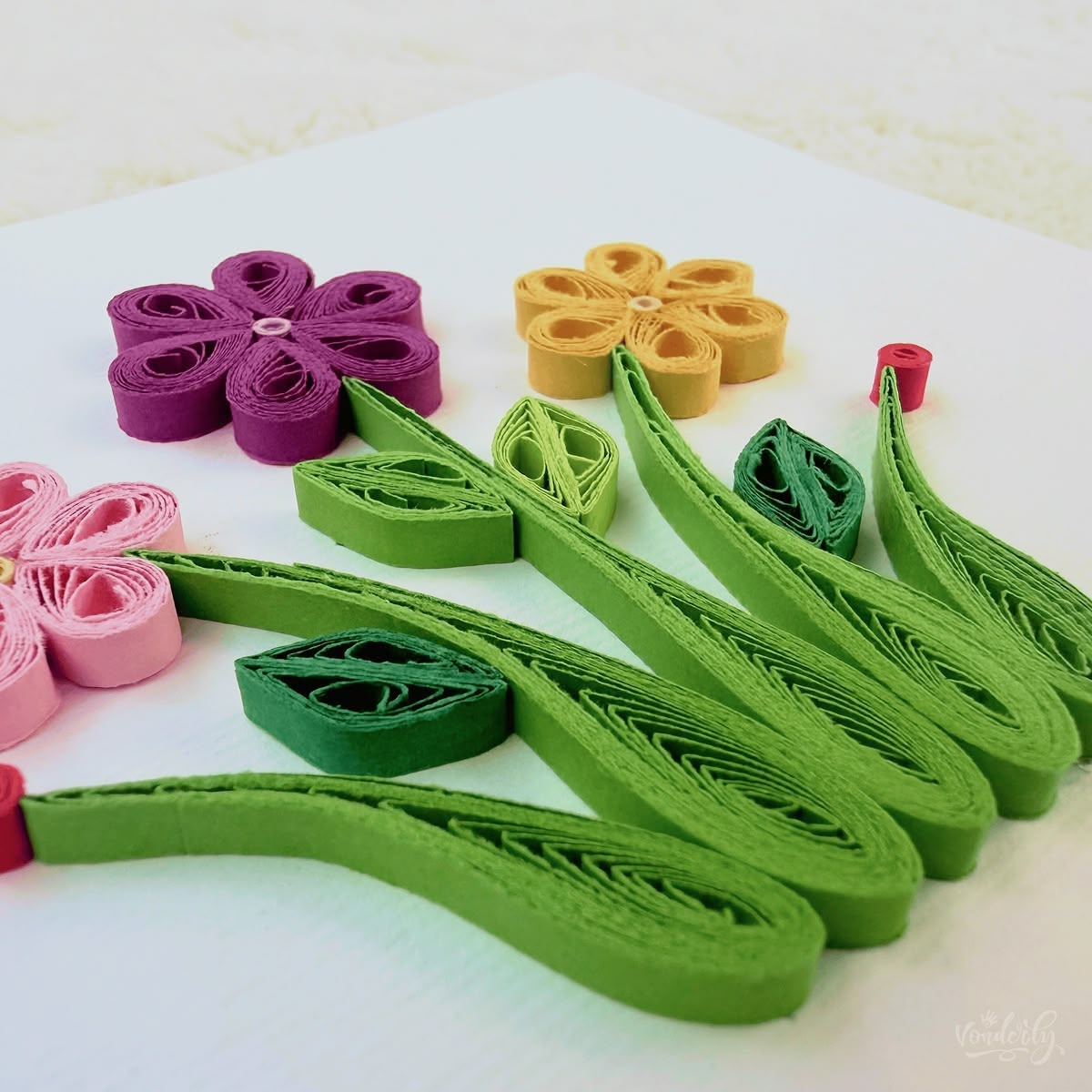 Angled view of quilled wildflowers card showing 3D raised paper art, six-petal flower loops and curving green stems visible