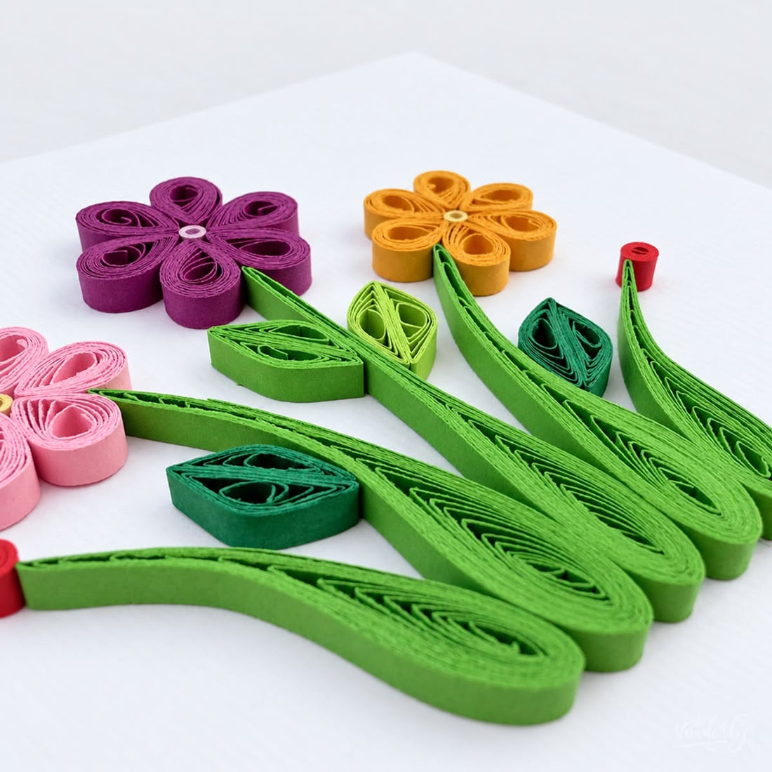 Wildflowers quilled greeting card with pink, purple, and yellow looped-petal flowers above green grass blades.