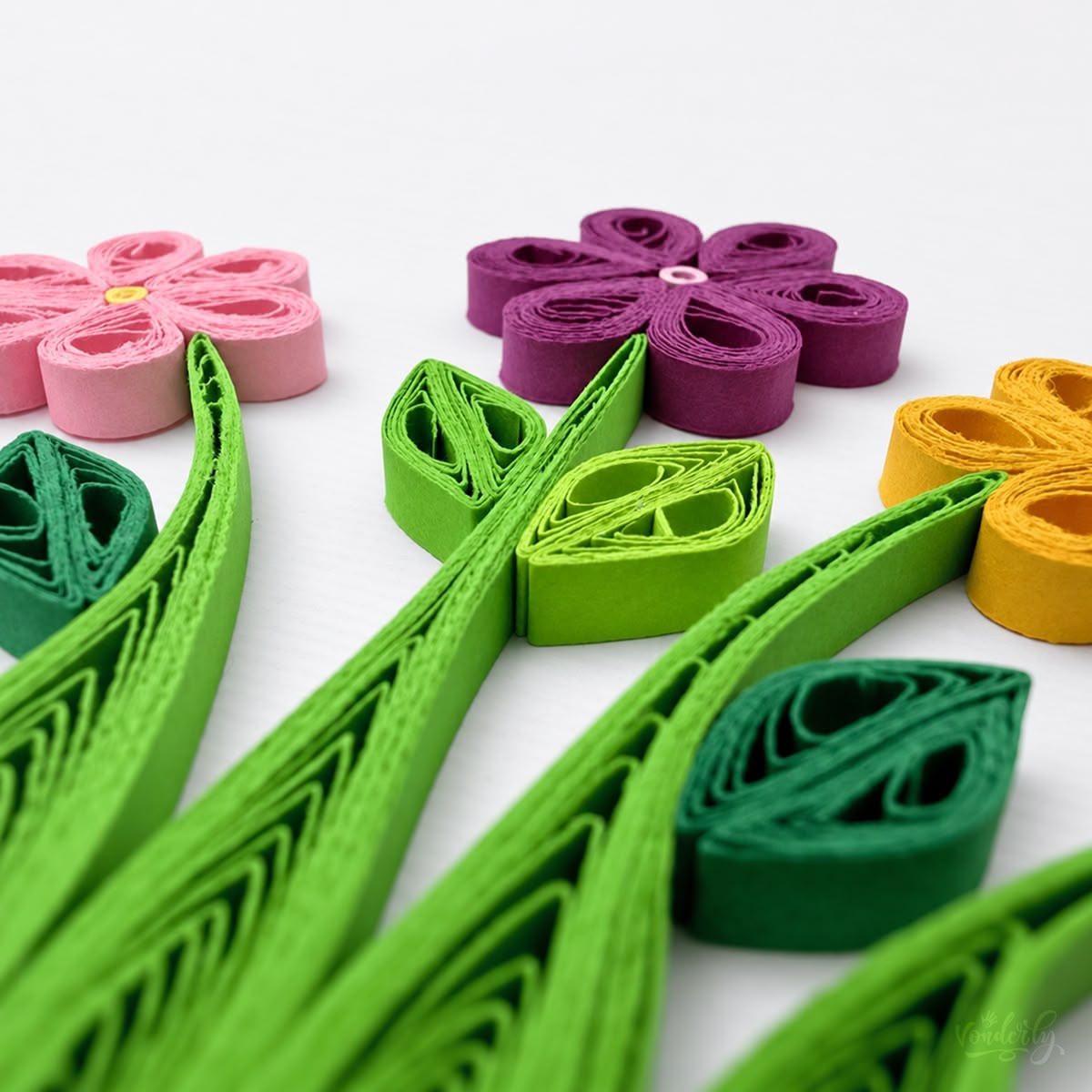 Close-up of pink, purple, and orange paper strips coiled into six-petal flowers with green leaves.