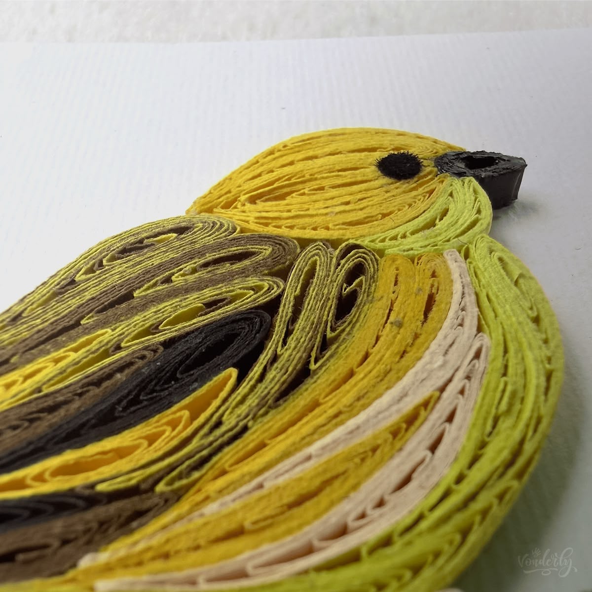 Close-up macro of paper quilling on yellow warbler card, three yellow tones layered with brown wing detail and cream belly
