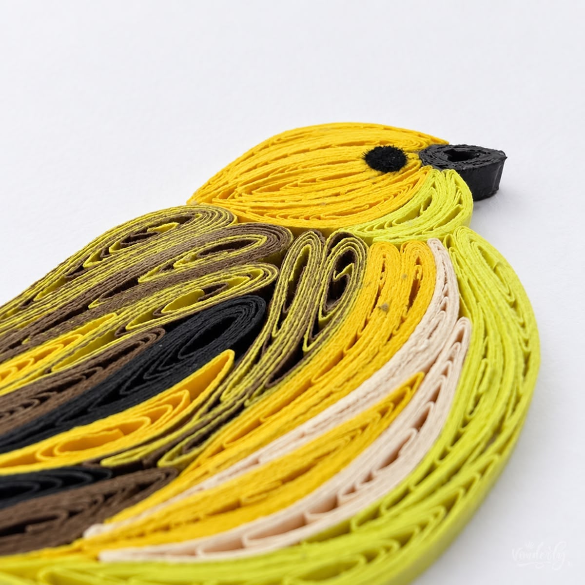 Close-up of golden yellow, lime, and cream paper strips forming the warbler's head and breast, with a black beak and eye.